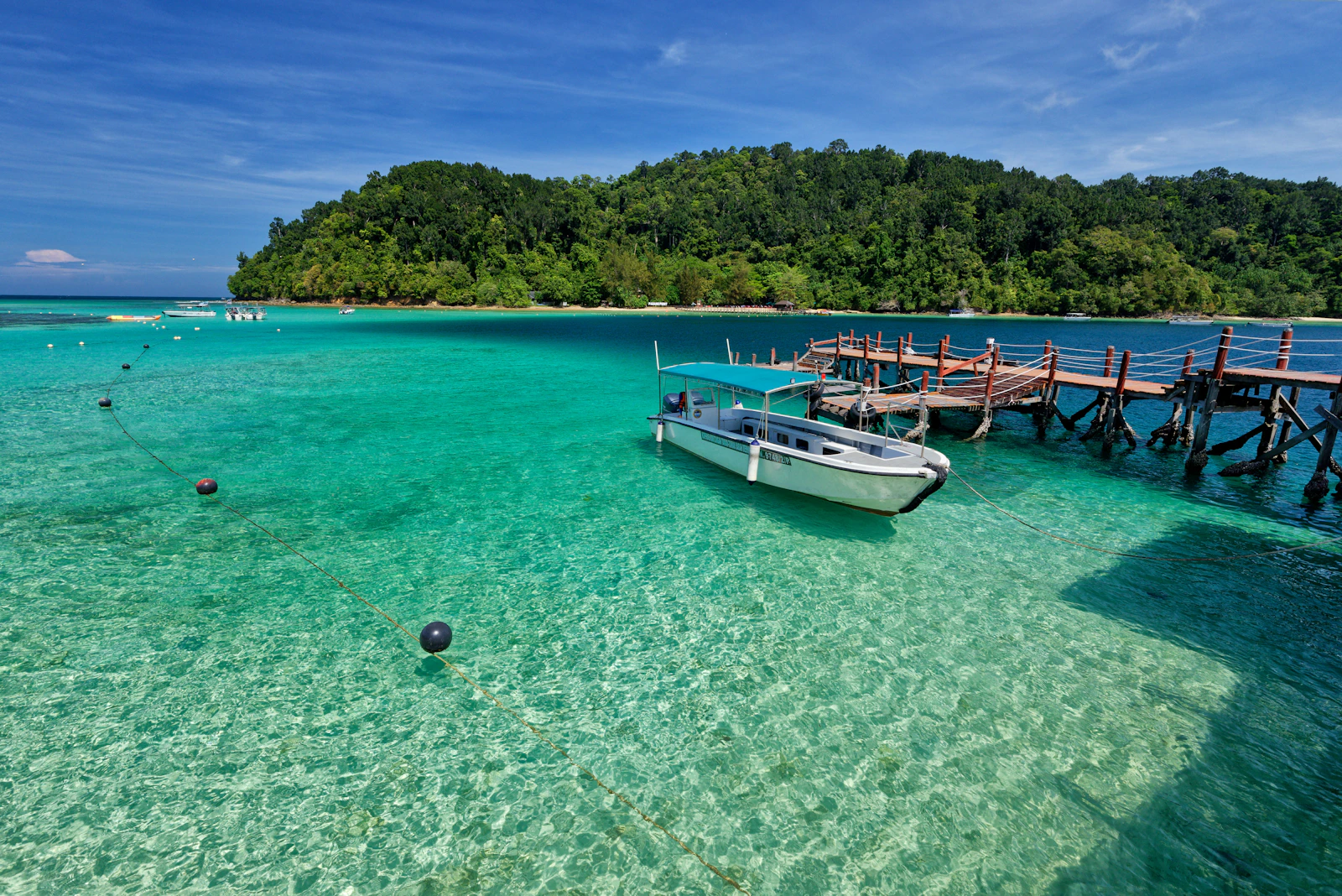 A small boat beside a wooden pier over clear turquoise water at Pulau Sapi, Sabah