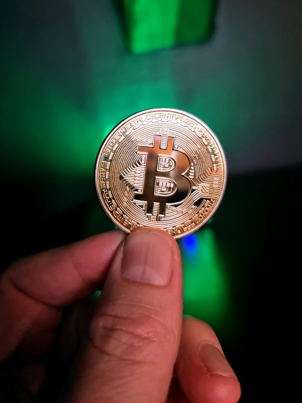 a hand holding a bit coin in front of a green light