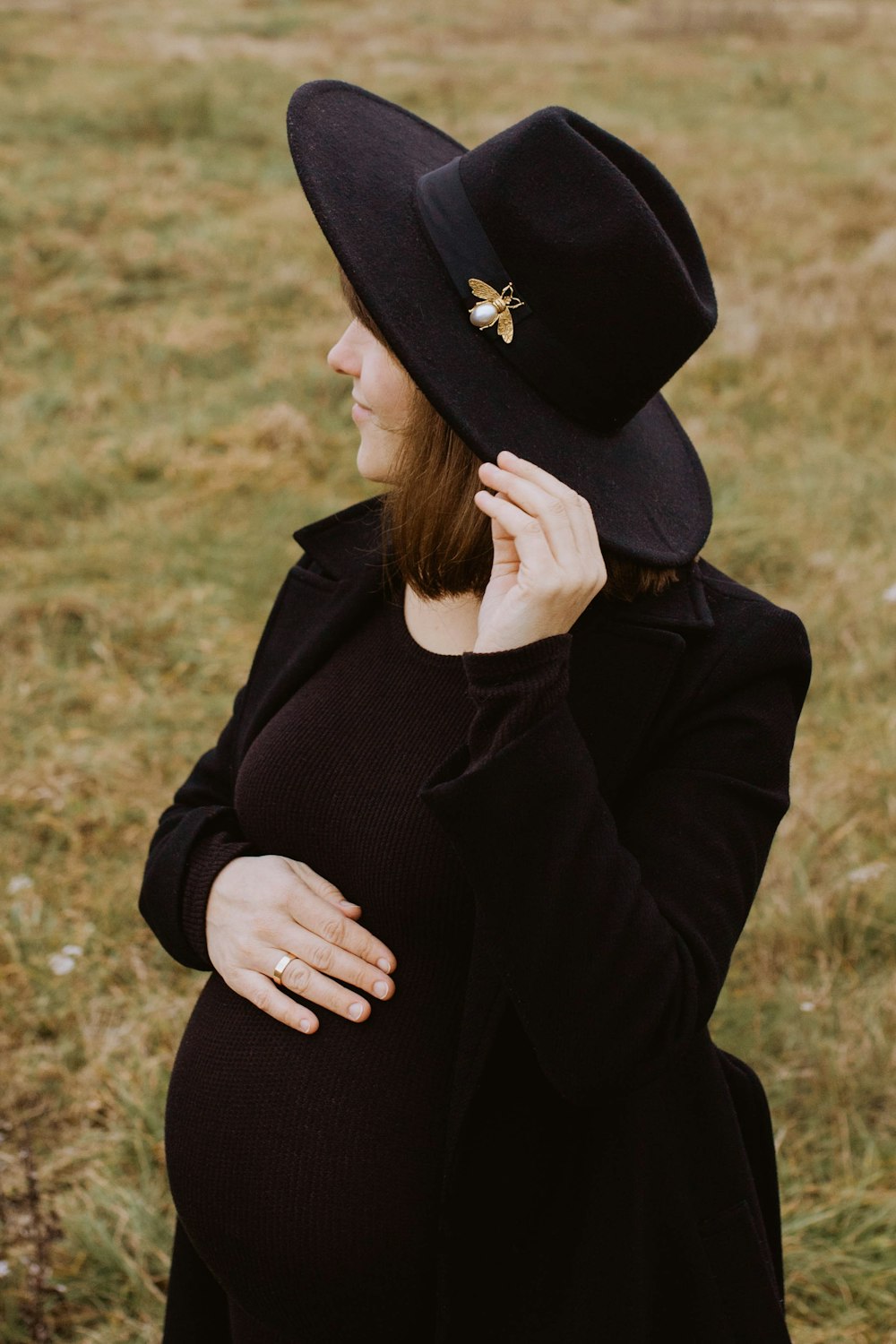 a pregnant woman wearing a black hat in a field