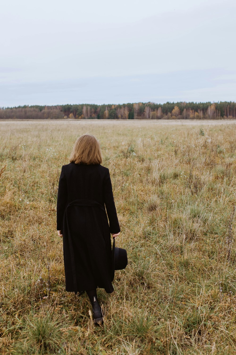 a woman in a black coat is walking through a field