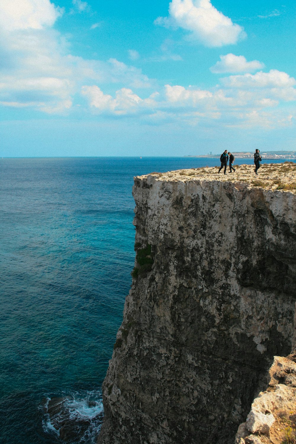 a group of people standing on top of a cliff next to the ocean