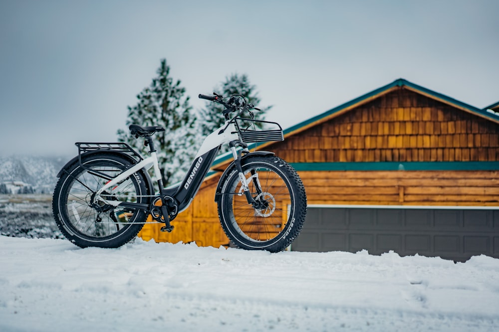 a bicycle parked in the snow in front of a cabin