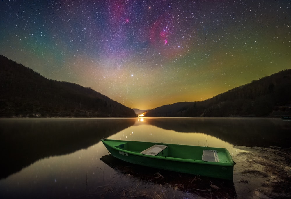 a green boat sitting on top of a lake under a night sky