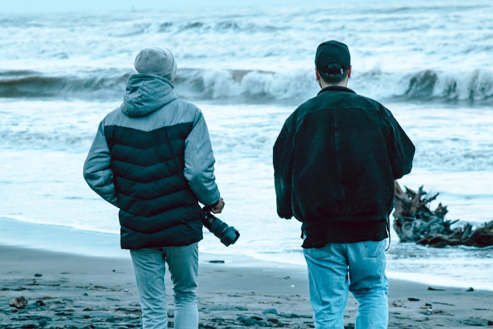 a couple of men walking along a beach next to the ocean