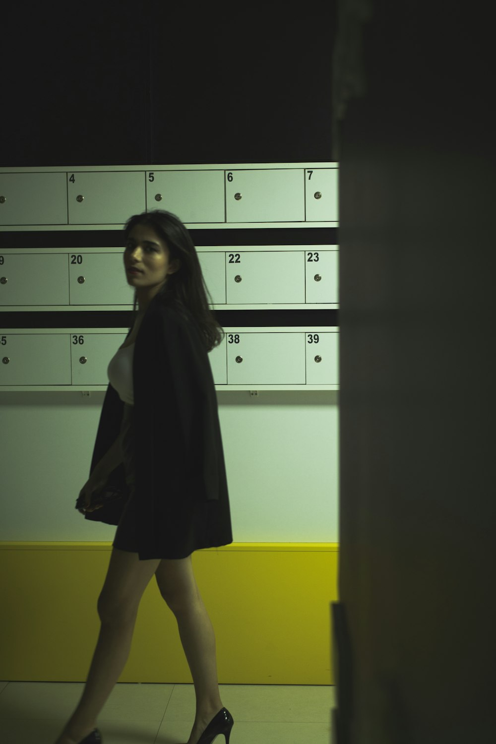 a woman in a black dress and heels walking in front of a mailbox