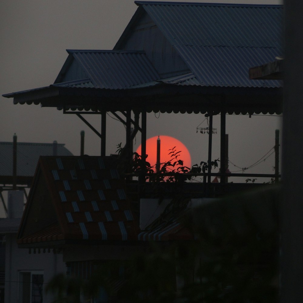 the sun is setting behind a building with a roof