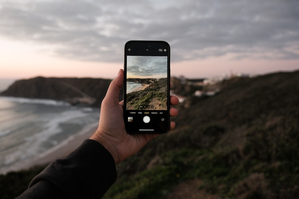 a person holding up a cell phone to take a picture of the ocean