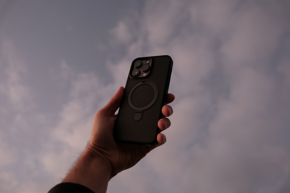 a hand holding a cell phone in front of a cloudy sky