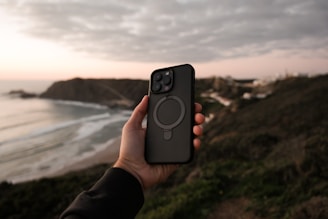 a person holding up a cell phone near the ocean