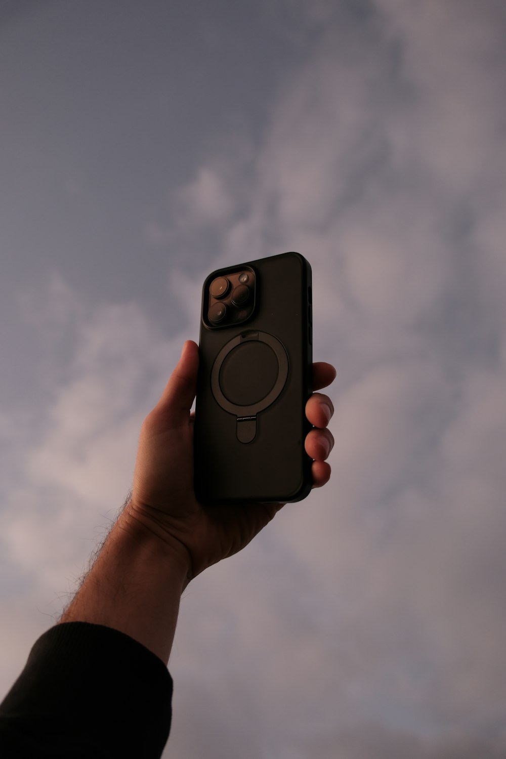a hand holding a cell phone with a sky in the background