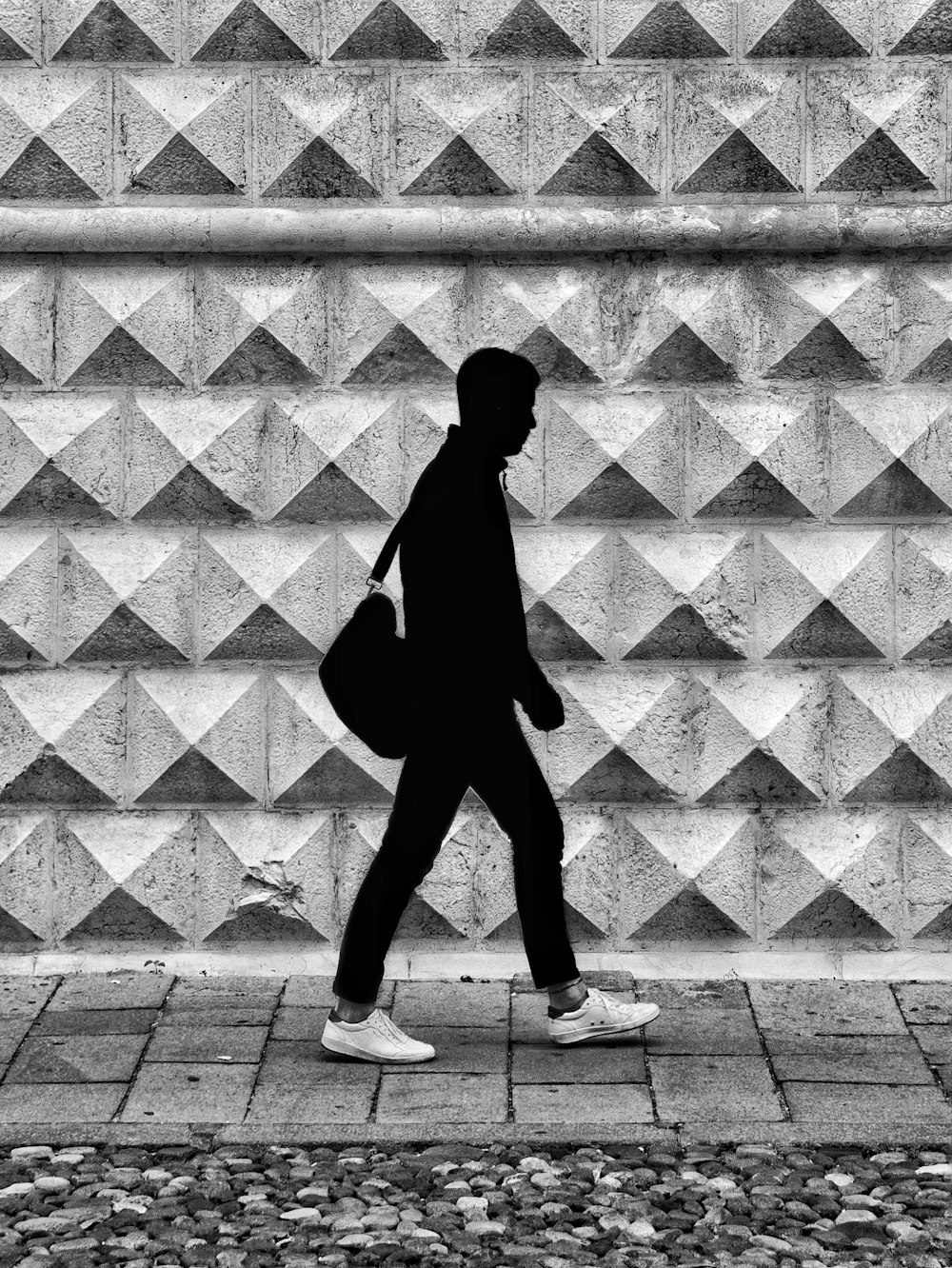 a black and white photo of a person walking past a wall