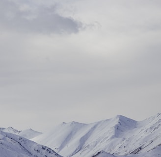 a mountain range covered in snow under a cloudy sky