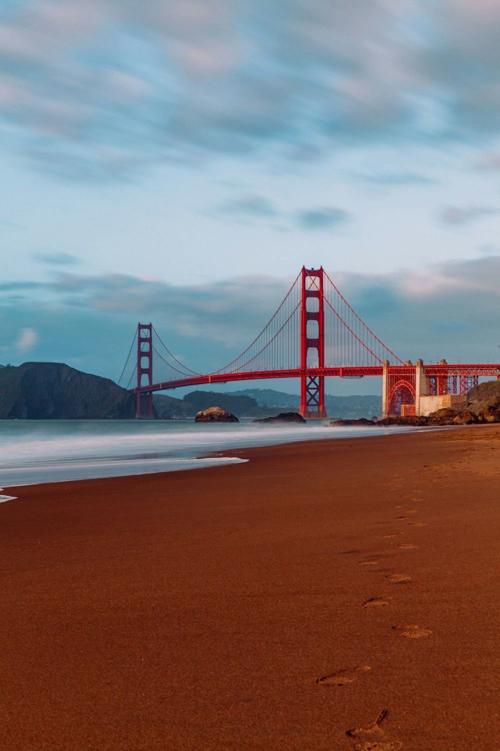 a beach with footprints in the sand and a bridge in the background