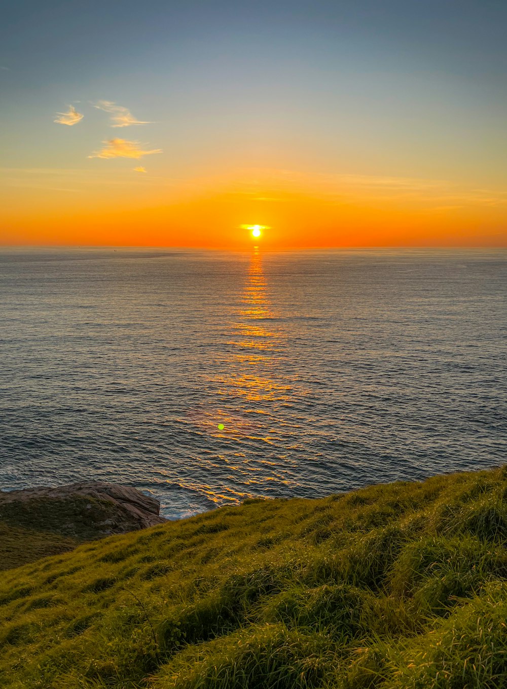 the sun is setting over the ocean on a grassy hill