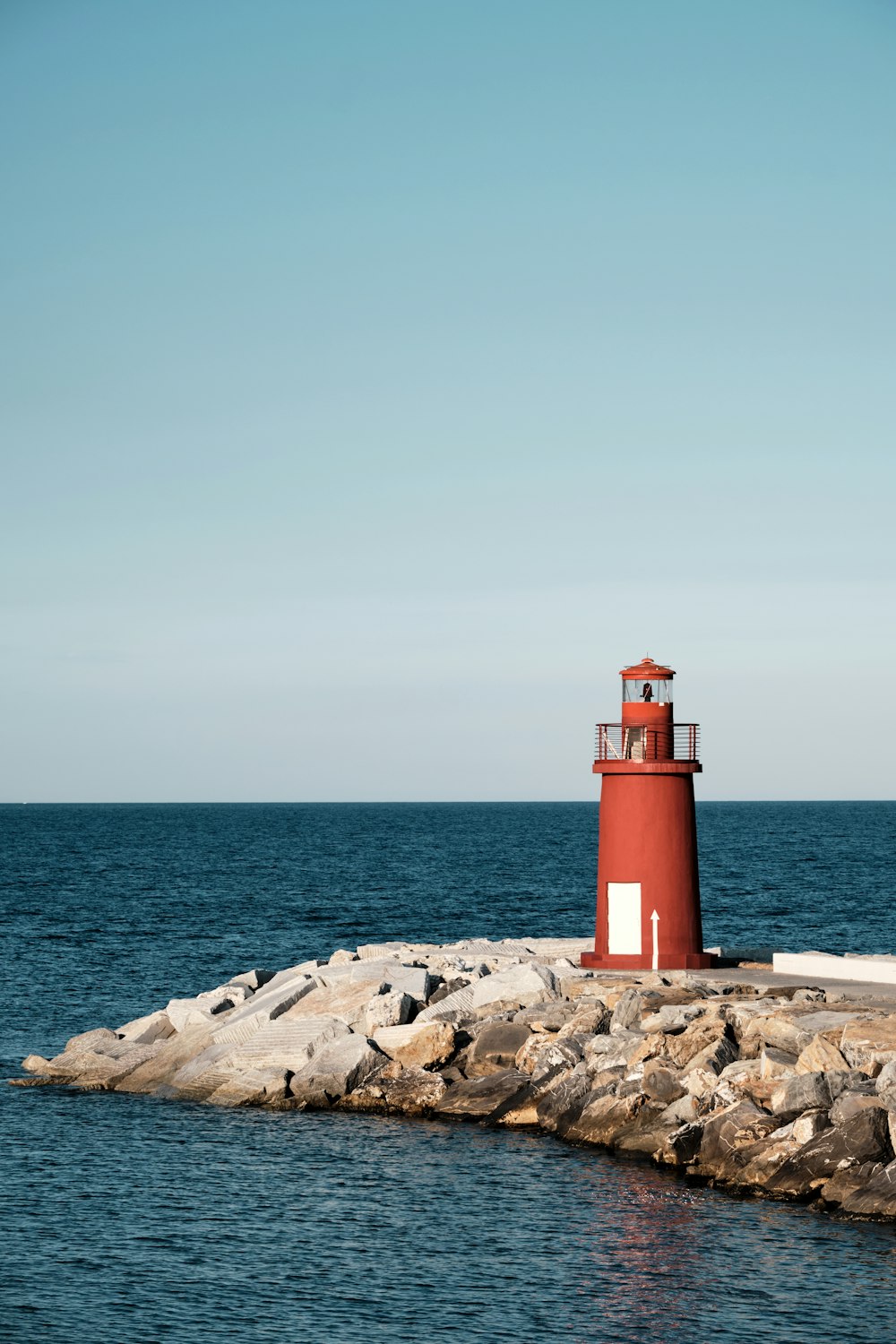 a red light house sitting on top of a rock pier