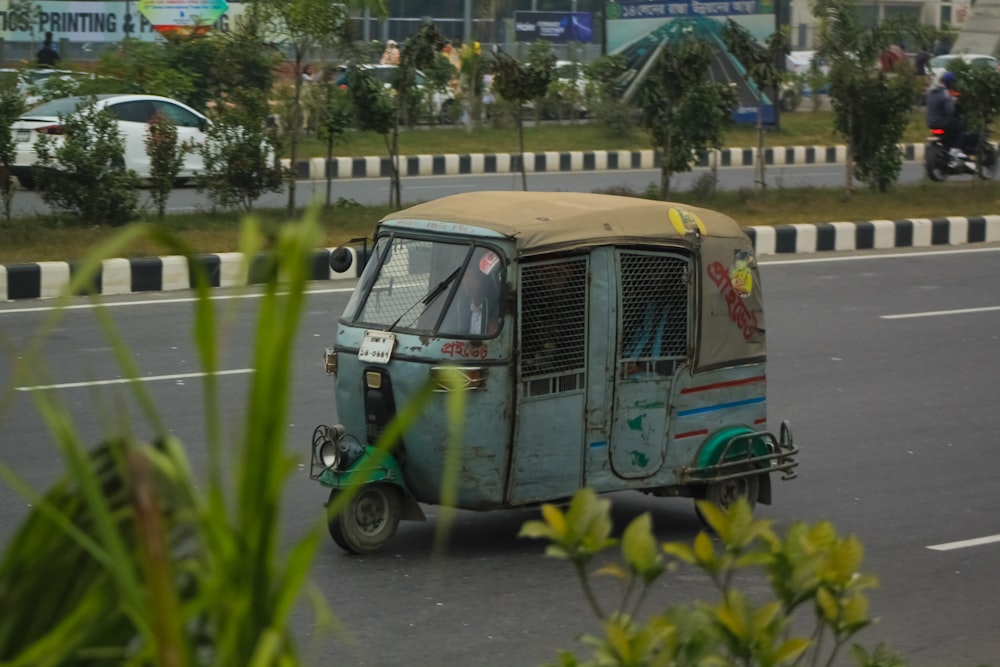 a small vehicle driving down a street next to a lush green field