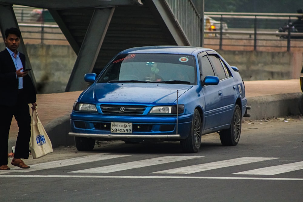 a blue car driving down a street next to a bridge