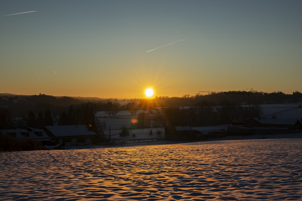 the sun is setting over a snowy field