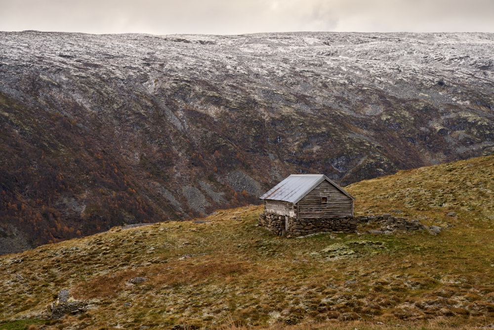 a small cabin on a grassy hill with mountains in the background