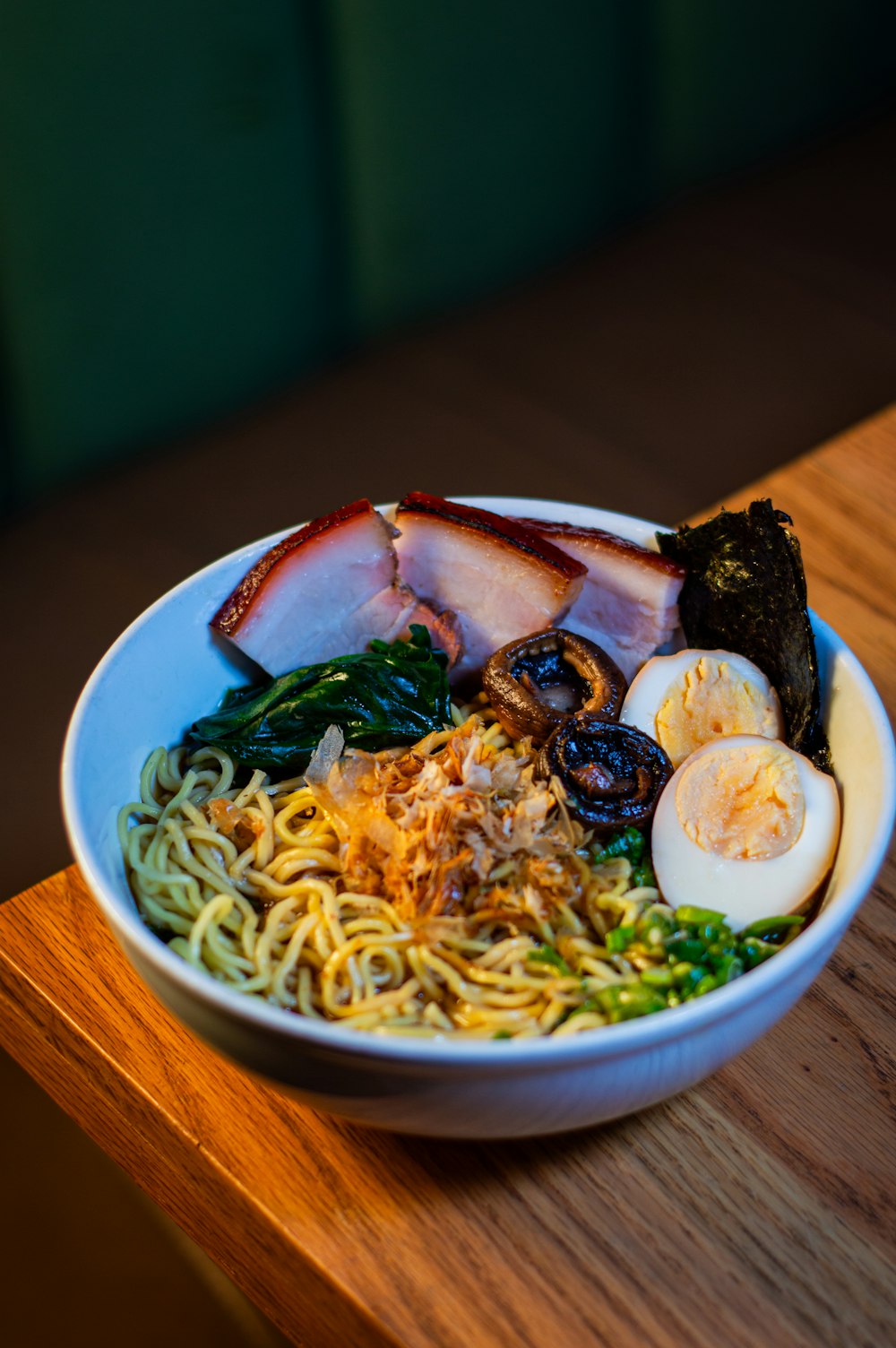 a bowl of noodles, meat, and vegetables on a wooden table
