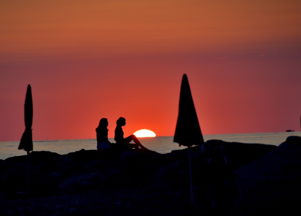 a couple of people sitting on top of a beach under umbrellas