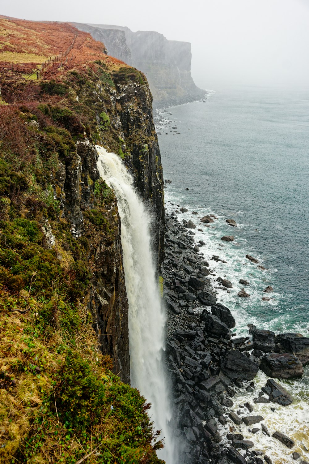 a waterfall flowing into the ocean next to a cliff