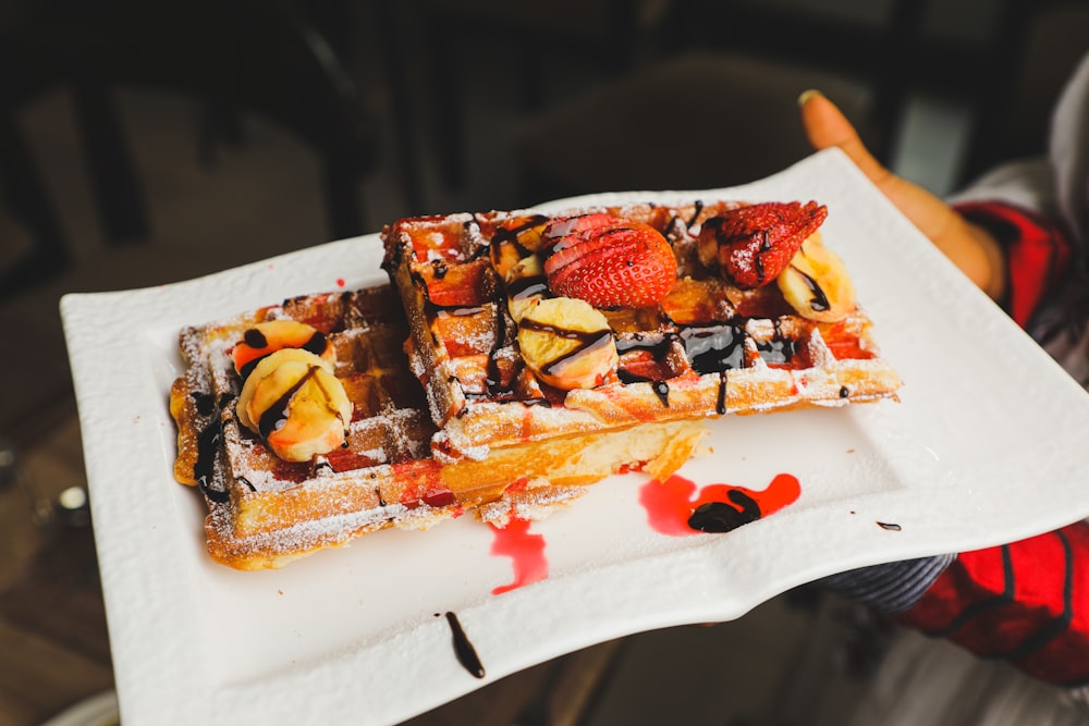 a person holding a plate of waffles covered in fruit