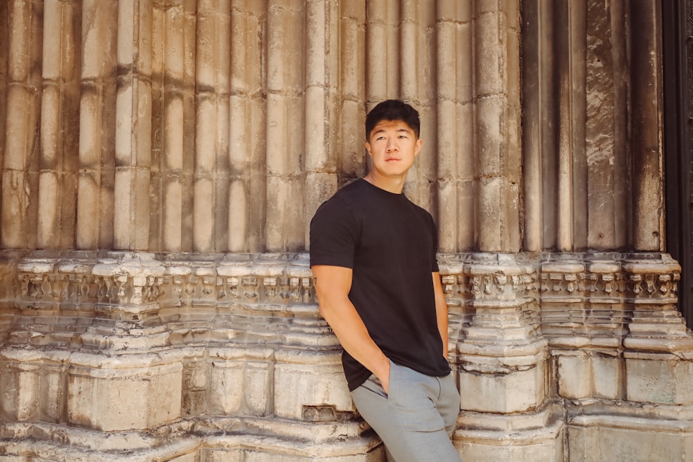 a young man leaning against a stone wall