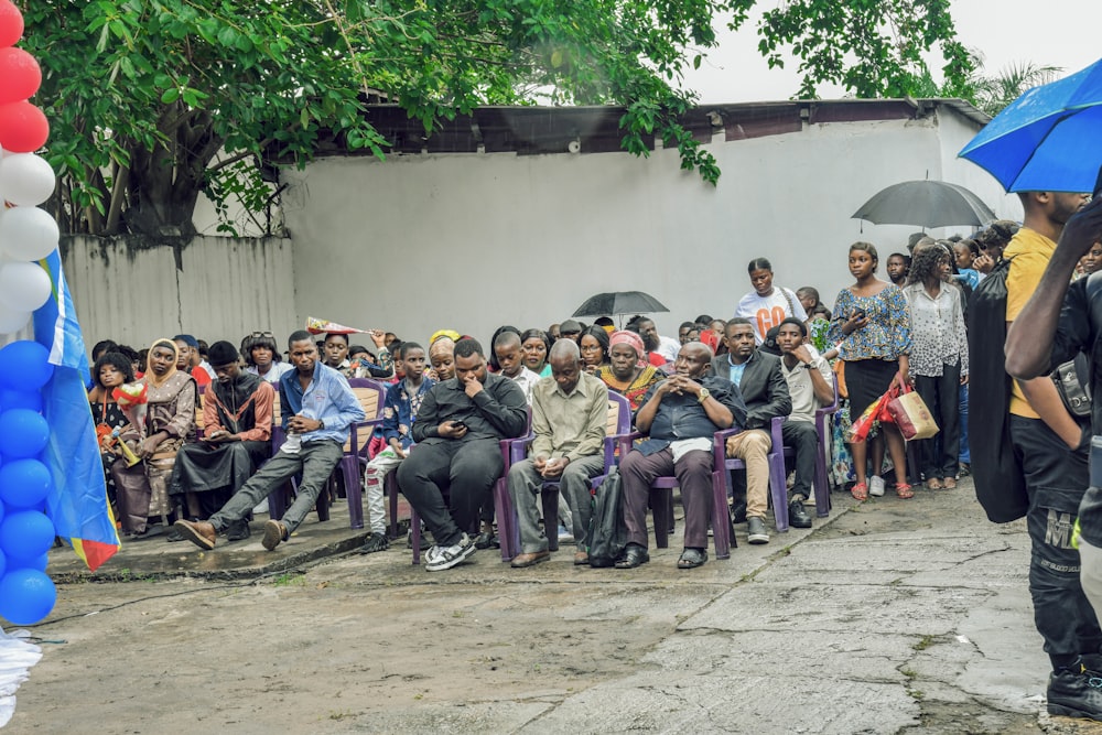 a group of people sitting in front of a crowd under umbrellas