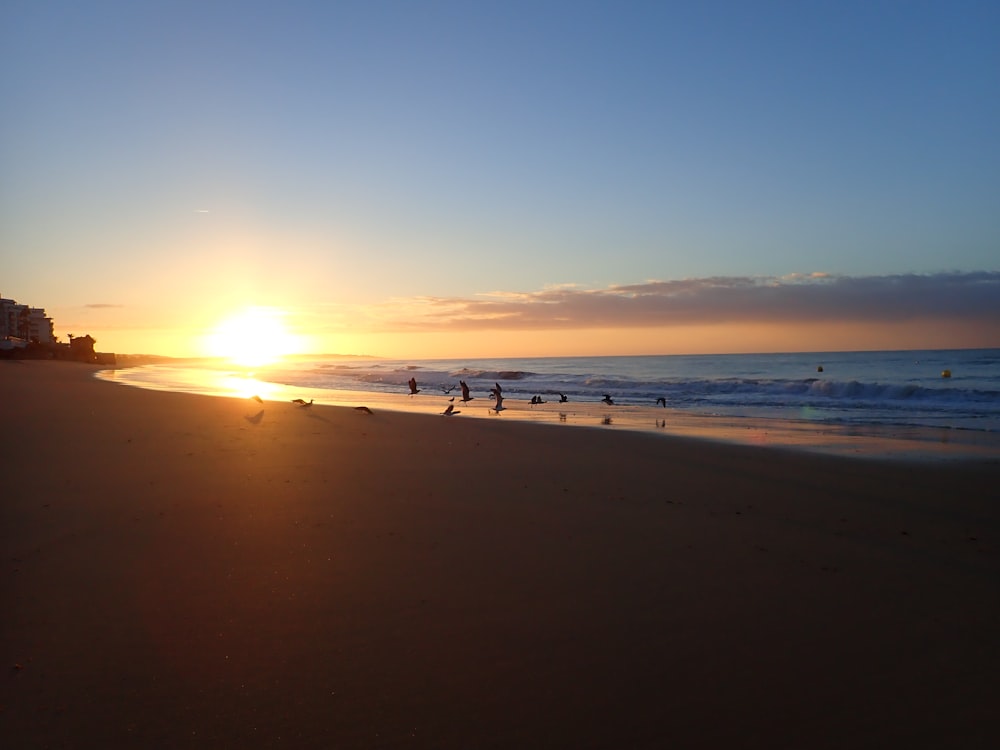 a sunset on a beach with people walking on the sand