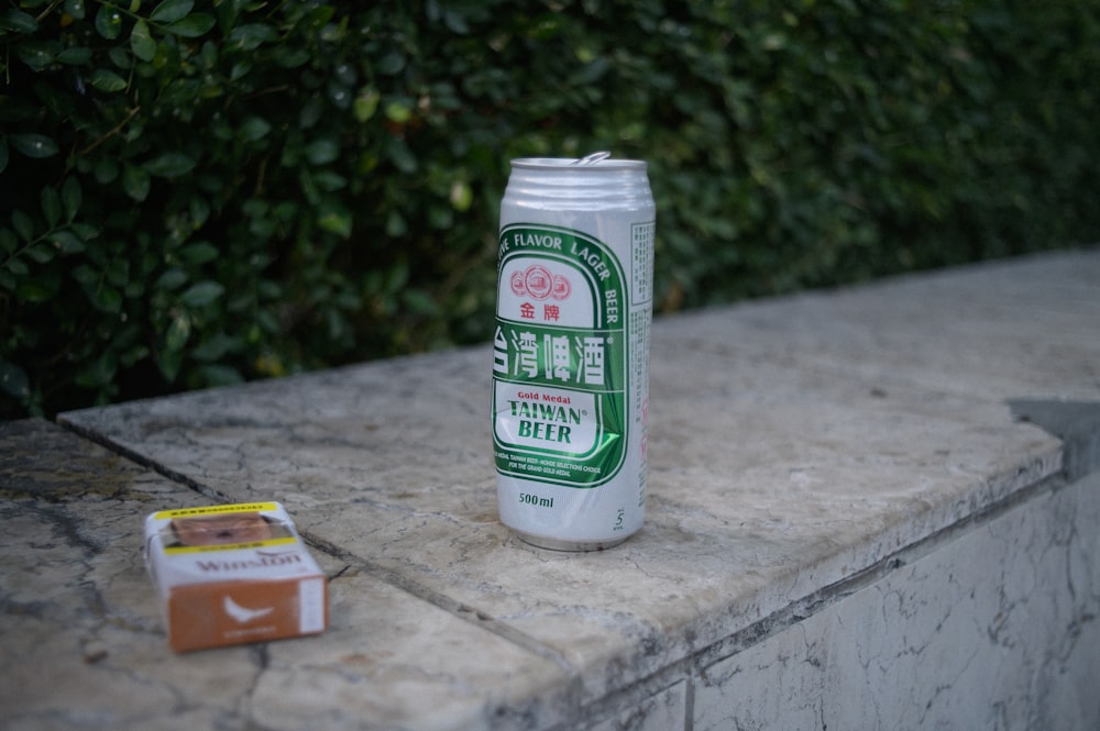 a can of beer sitting on a ledge next to a pack of cigarettes