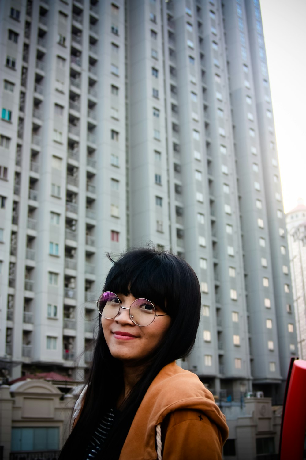 a woman wearing glasses standing in front of a tall building