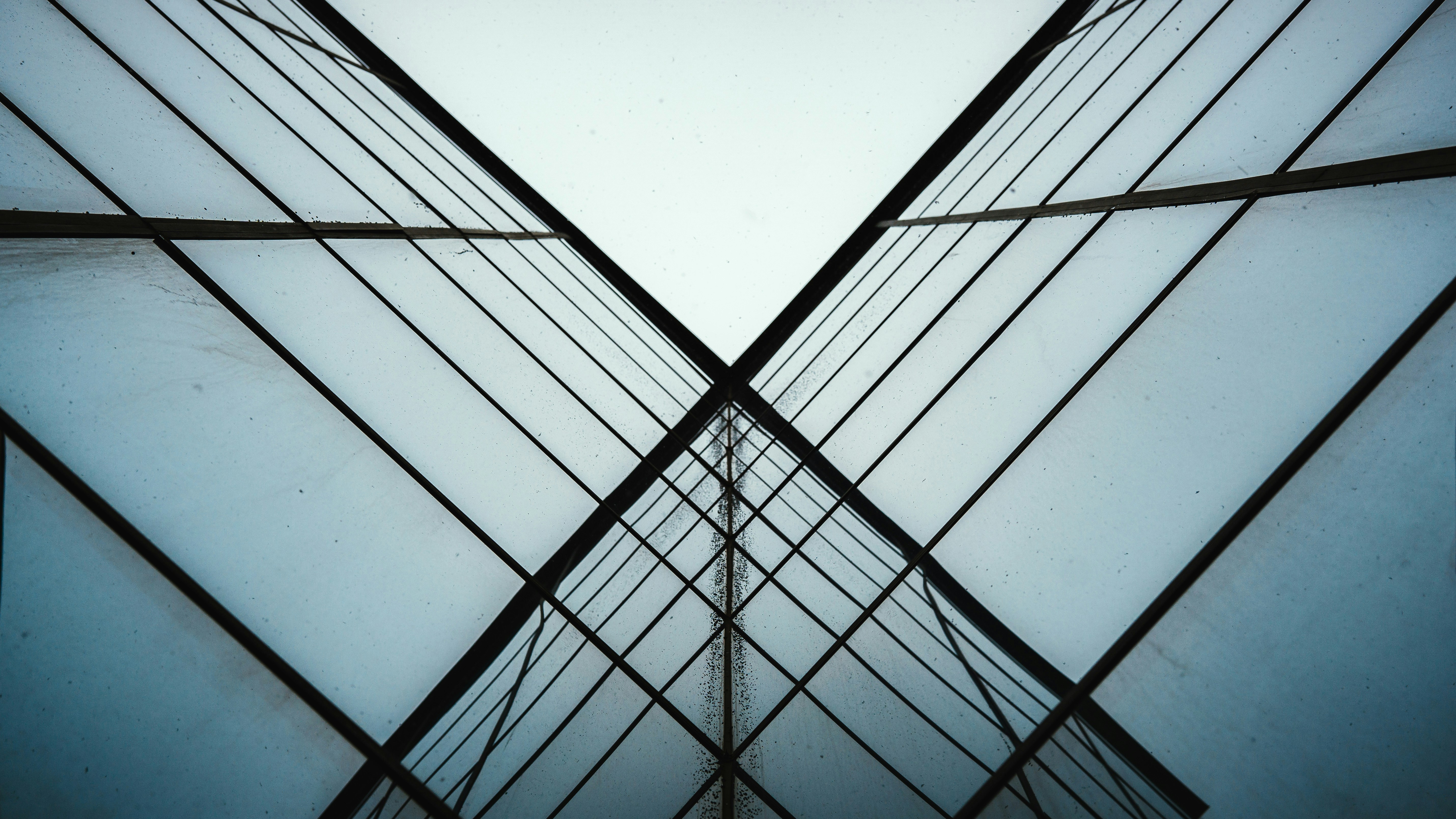 Symmetrical view of glass windows forming an X-shaped pattern, reflecting the sky.
