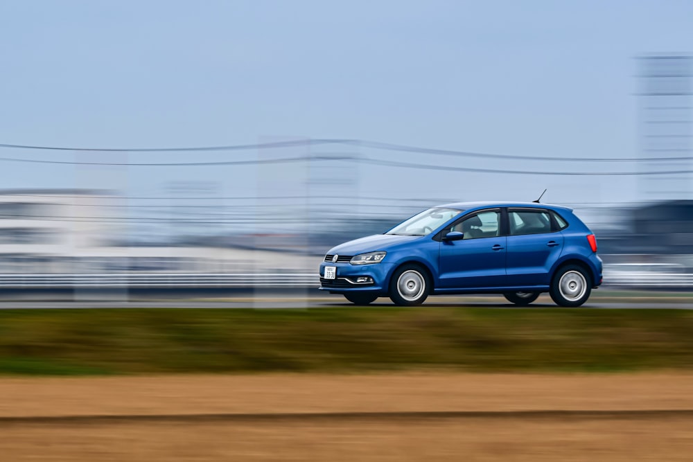 Un coche azul conduciendo por una carretera junto a un campo