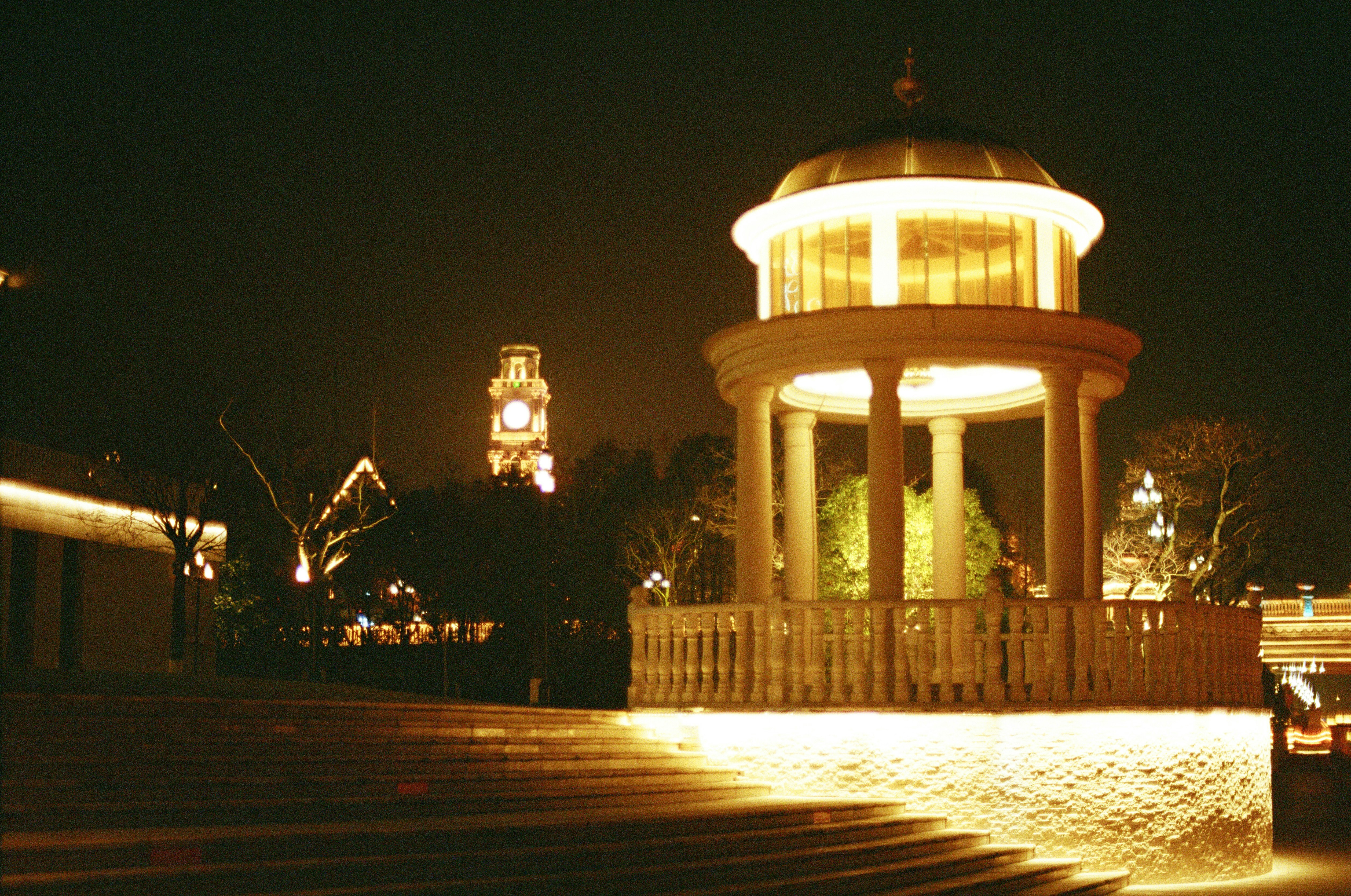 a gazebo lit up at night with a clock tower in the background