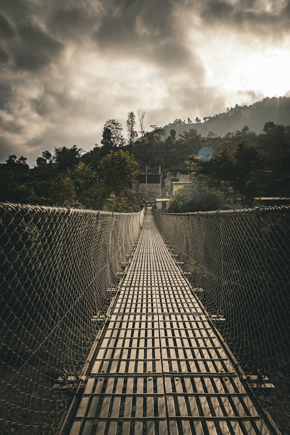 a long suspension bridge over a river under a cloudy sky