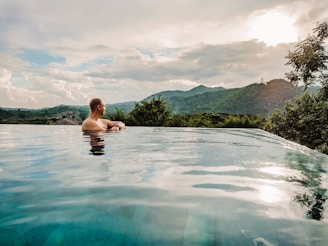 a man sitting in a swimming pool with mountains in the background