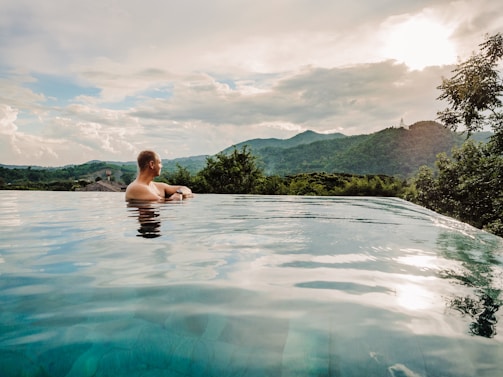 a man sitting in a swimming pool with mountains in the background