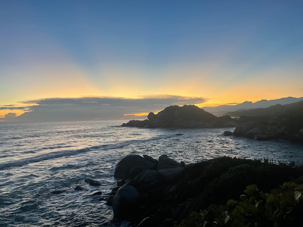 El sol se está poniendo sobre el océano con rocas en primer plano