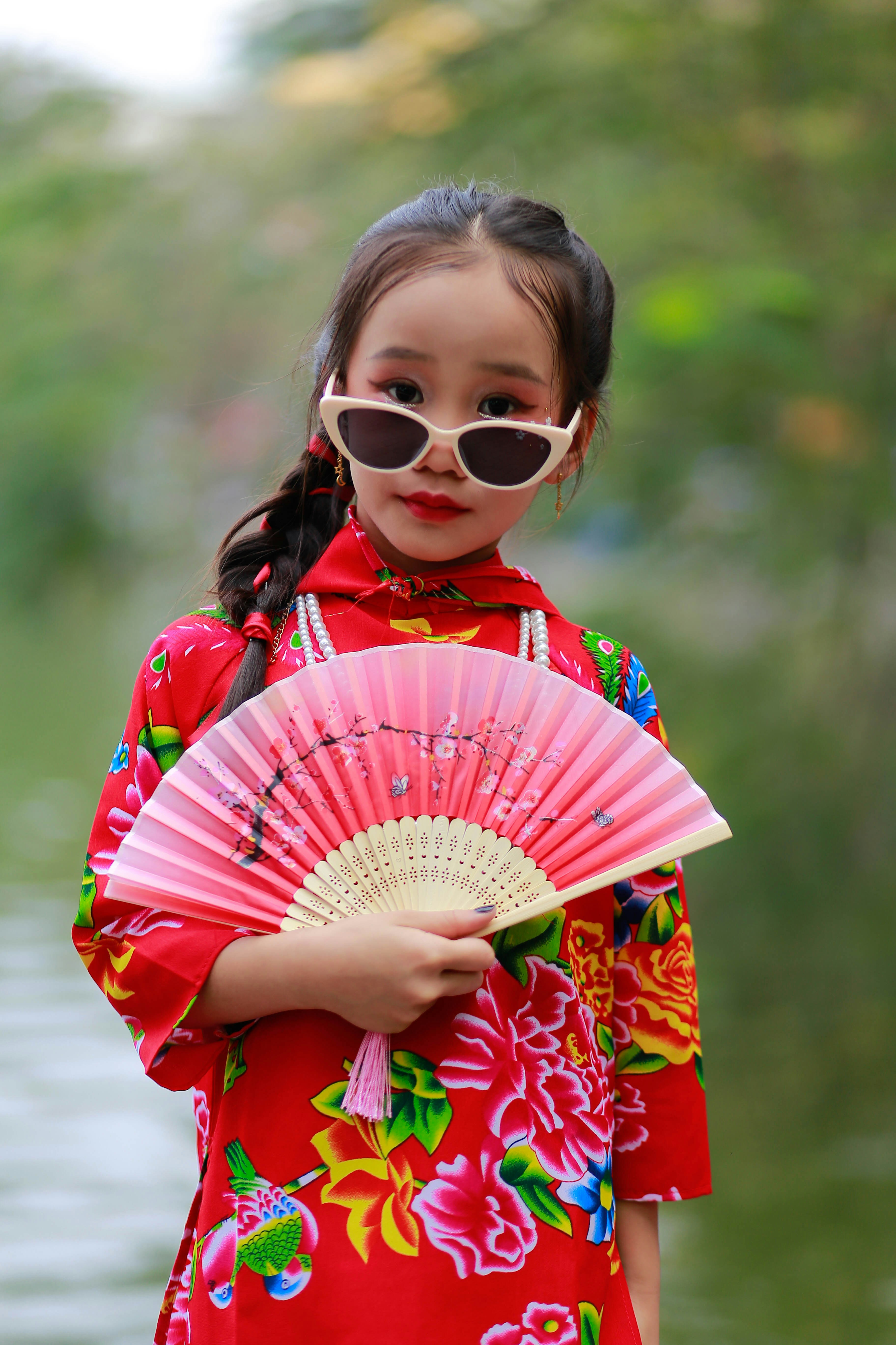 a little girl in a red dress holding a pink fan