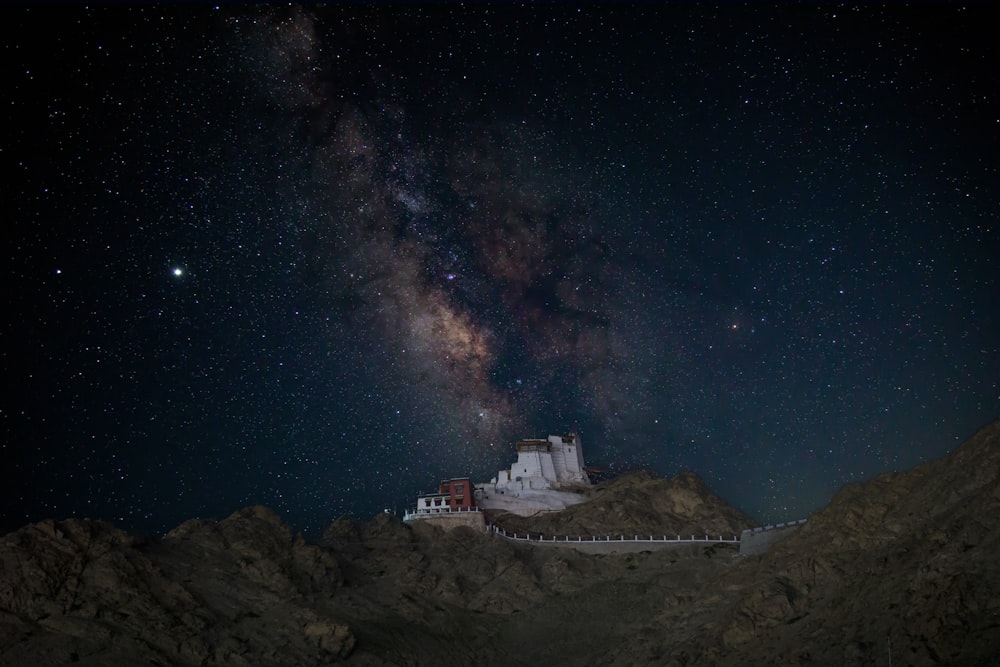 a night view of a mountain with a building in the foreground and the milky