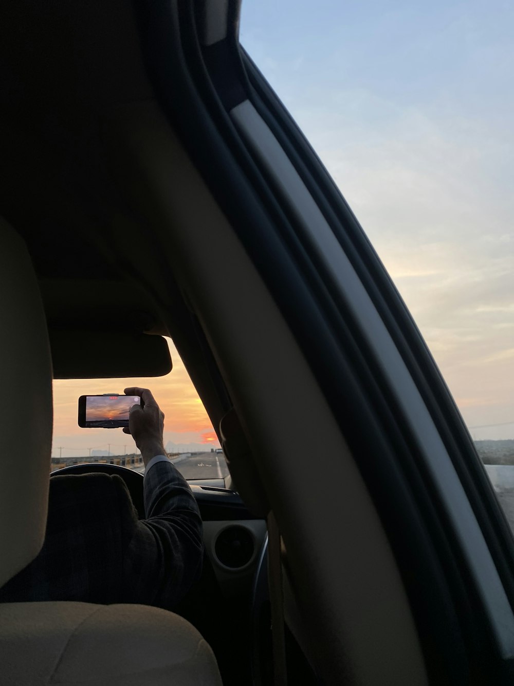 a person taking a picture of the sun setting in a car