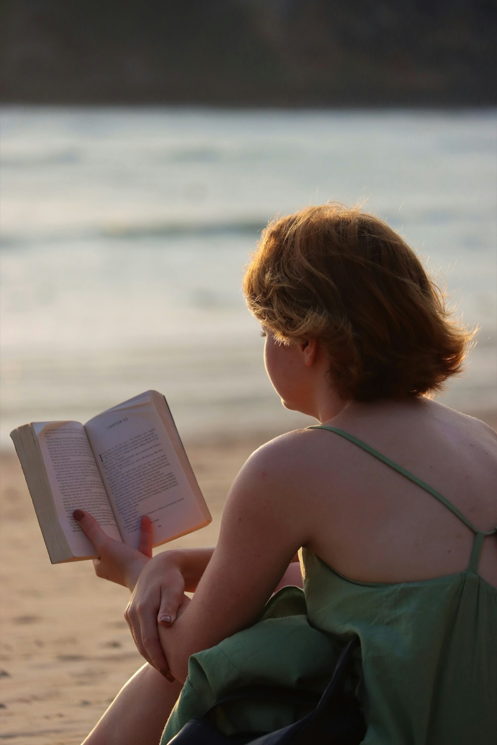 a woman sitting on a beach reading a book