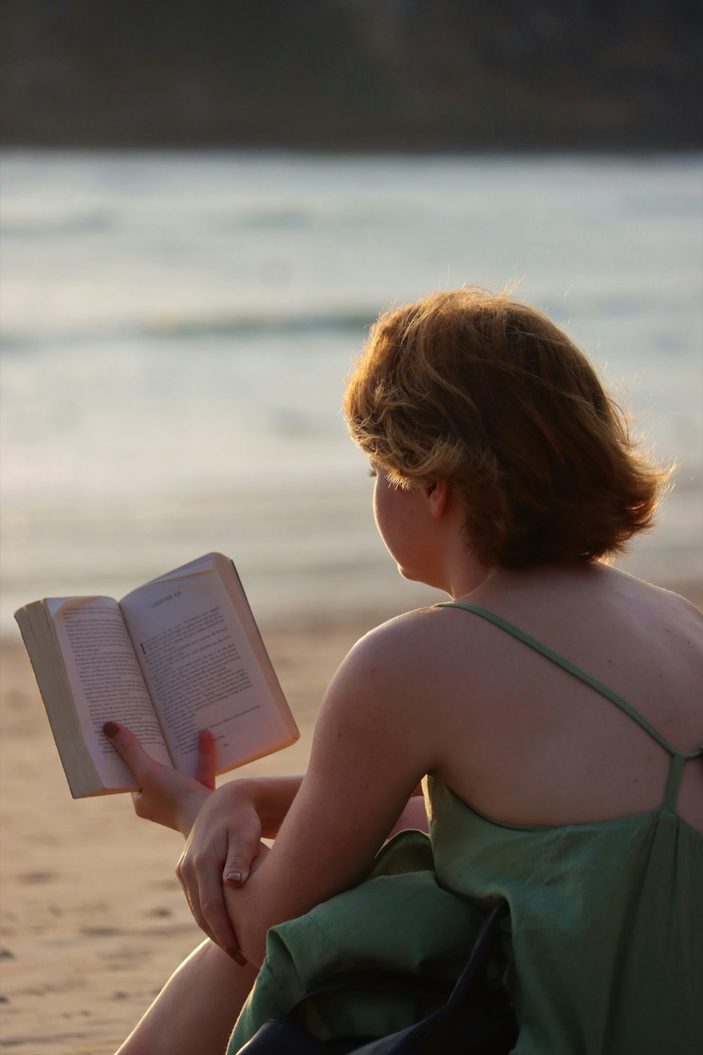 eine Frau sitzt am Strand und liest ein Buch