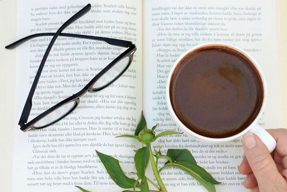 una persona che tiene una tazza di caffè davanti a un libro aperto