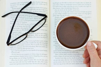 a person holding a cup of coffee in front of an open book