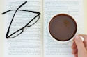 a person holding a cup of coffee in front of an open book