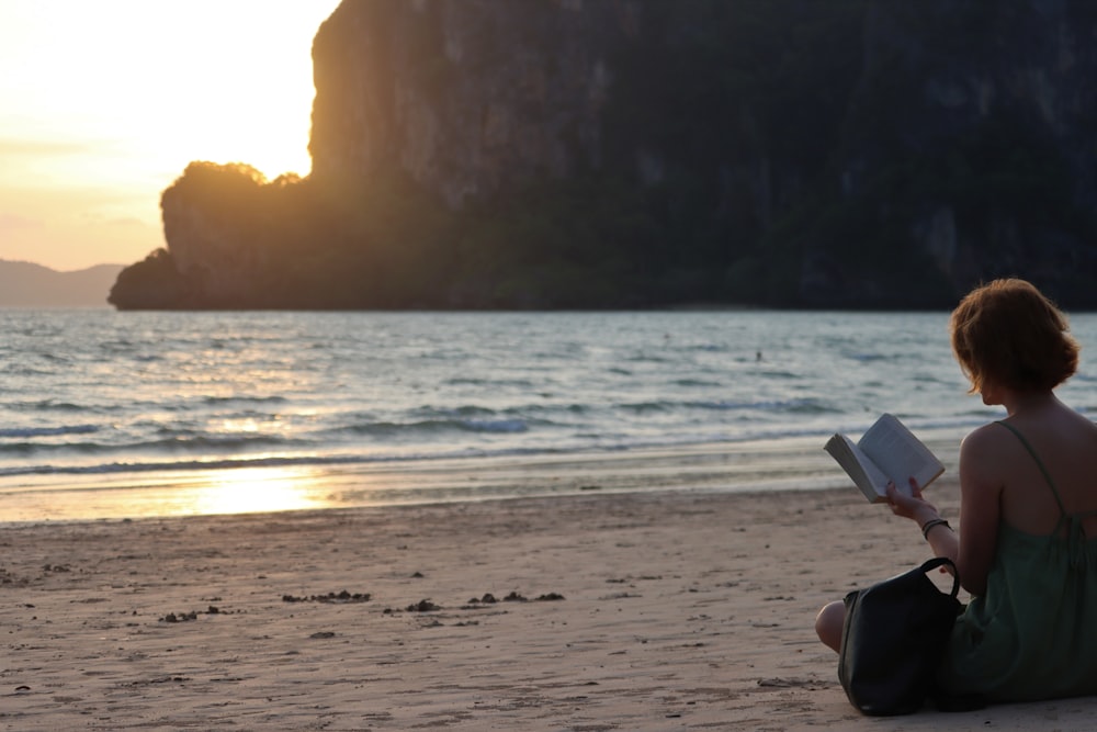 a woman sitting on a beach reading a book