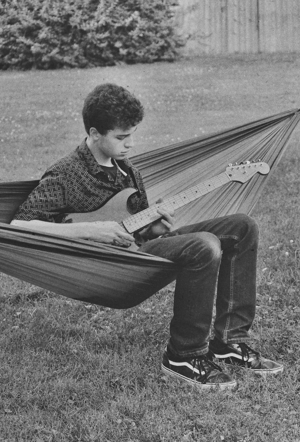 a boy sitting in a hammock playing a guitar