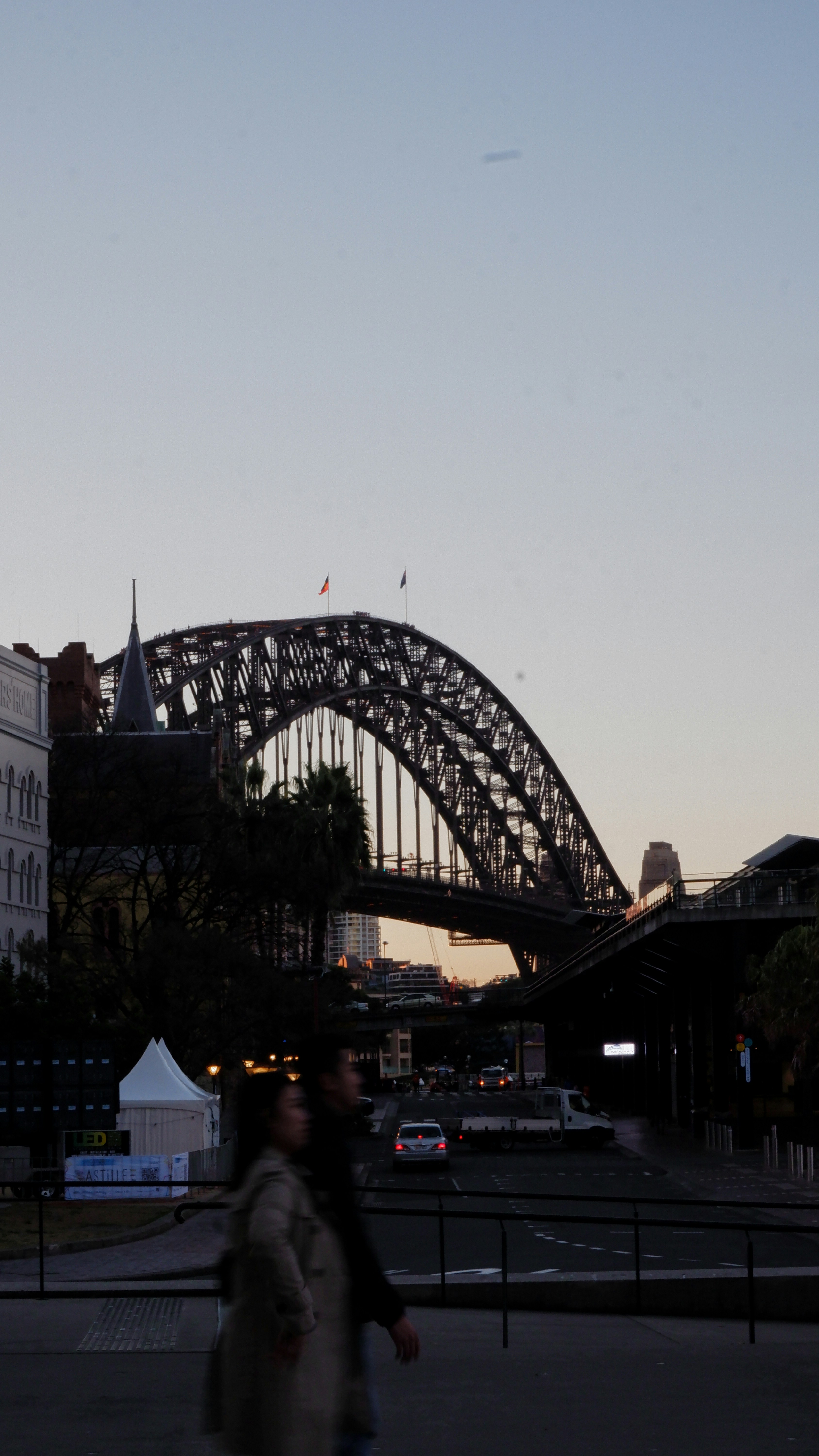 a couple of people walking across a street next to a bridge